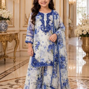 May include: A three-piece outfit consisting of a long-sleeved tunic, wide-leg trousers, and a matching dupatta. The set features a white base with a blue floral print, accented by dark blue lace embroidery on the neckline and hem edges.