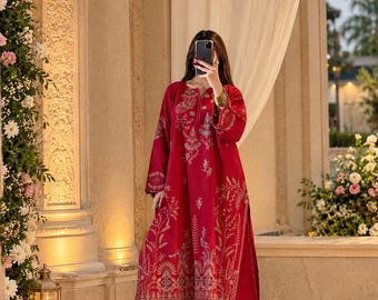 May include: A deep red long-sleeved tunic and matching wide-leg trousers set featuring intricate gold-toned embroidery along the neckline, sleeves, and hemline. The garment has a scalloped edge detail on the tunic and pant cuffs.
