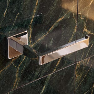 Peut inclure: Un porte-papier toilette en chrome poli doté d'une base carrée fixée au mur et d'un bras horizontal avec une petite extrémité relevée. La finition métallique reflète la lumière, mettant en valeur un design angulaire fixé sur un mur en marbre vert.