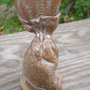 May include: A handmade, brown ceramic chalice with a textured surface and a unique, organic shape. The chalice has a wide bowl and a narrow stem, with light-colored accents. The chalice is approximately 4 inches tall.