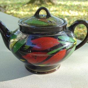 Pode incluir: Uma chaleira preta com tampa, pintada com desenhos florais vermelhos, verdes e amarelos.