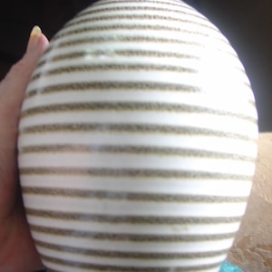 Op de afbeelding: Een witte keramische vaas met bruine strepen. De vaas heeft een rond lichaam en een smalle hals.