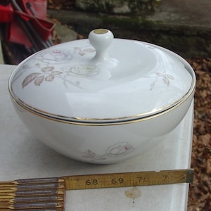 May include: White porcelain bowl with a lid, featuring a delicate floral design of roses and leaves in shades of gray and pink. The bowl has a gold trim around the rim and a gold knob on the lid.