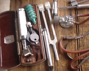 May include: A brown leather case with a set of medical instruments, including a stethoscope, a tuning fork, and an otoscope. The case is open and the instruments are visible.