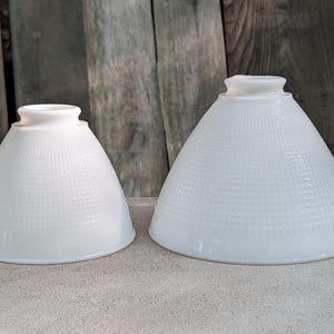 May include: Two white glass lamp shades with a conical shape and a textured grid pattern. Each shade features a smooth, circular opening at the top for mounting and a wider, flared base. The glass has a semi-translucent, milk-white finish.