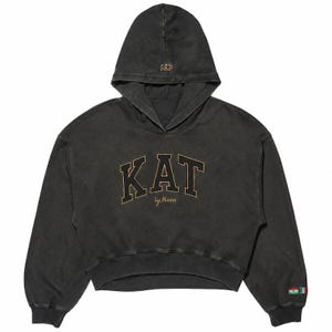 May include: A charcoal black cropped hoodie featuring a hood with the text GAP embroidered in gold. The front displays the text KAT in large gold-outlined letters with the words by Mason underneath. A small flag patch is on the left sleeve cuff.