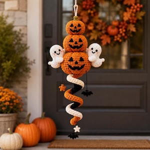 May include: A hanging crochet decoration featuring three stacked orange jack-o'-lanterns with black stitched faces, flanked by two small white ghosts. Below, a spiral tail in orange, black, and white hangs with small star and bat accents.
