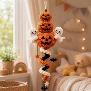May include: A hanging crochet decoration featuring three stacked orange jack-o'-lanterns with black stitched faces, flanked by two small white ghosts. Below, a spiral tail in orange, black, and white hangs with small orange stars, white stars, and black bats.