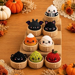 Puede incluir: Una colección de ocho pequeñas figuras redondas de ganchillo con temática de Halloween, cada una en una cesta de ganchillo color canela. Las figuras incluyen un esqueleto, un murciélago, un gato negro, un caramelo de maíz, una momia, una araña, un monstruo verde y una manzana roja.