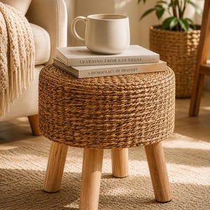 May include: A round stool featuring a woven natural fibre top and four light-coloured wooden legs. Two books titled Learning from Las Vegas and A Democracy of Imagery are stacked on the stool, topped with a plain off-white ceramic mug.