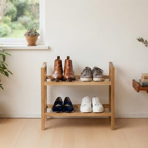 Pode incluir: Uma sapateira de dois níveis em madeira clara com um design de estrutura simples. A prateleira superior contém um par de botas de couro castanho e um par de ténis cinzentos. A prateleira inferior contém mocassins azul-escuro e ténis brancos.