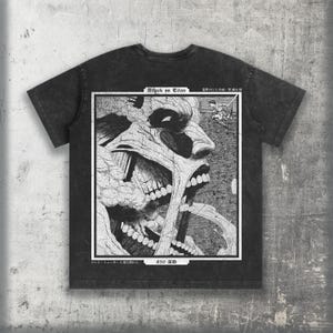 May include: A charcoal black short-sleeve t-shirt featuring a large rectangular graphic print on the back. The print displays a detailed black and white illustration of a titan, the text Attack on Titan, and Japanese characters.