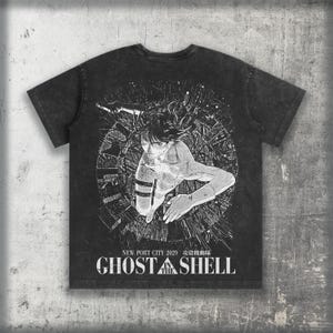 Könnte beinhalten: Ein anthrazitfarbenes Kurzarm-T-Shirt mit einem weißen Grafikdruck einer Figur in einem kreisförmigen digitalen Netzwerk. Der Text lautet NEW PORT CITY 2029 und GHOST IN THE SHELL, ergänzt durch japanische Schriftzeichen unter dem Stadtnamen.