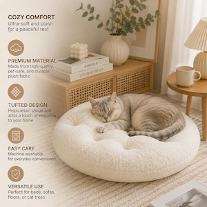 Puede incluir: Una cama redonda para mascotas de color crema, capitonada y hecha de tela de felpa. La cama presenta un diseño capitonado con botones y se muestra con un gato atigrado gris durmiendo encima. El texto en la imagen incluye COZY COMFORT, PREMIUM MATERIAL, TUFTED DESIGN, EASY CARE y VERSATILE USE.