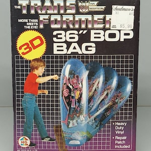 May include: A box for a 36-inch Transformers Bop Bag. The box features a 3D image of a Transformer character on a blue and purple inflatable bag. The box is black with yellow and red accents. The text on the box reads "Transformers 36" Bop Bag".