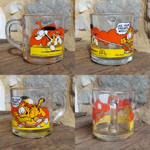 May include: Four clear glass mugs with a Garfield cartoon character design. The mugs feature a red, orange, and yellow color scheme. The text on the mugs reads "Use your friends wisely." and "Garfield Characters &copy;1978 United Feature Syndicate, Inc."