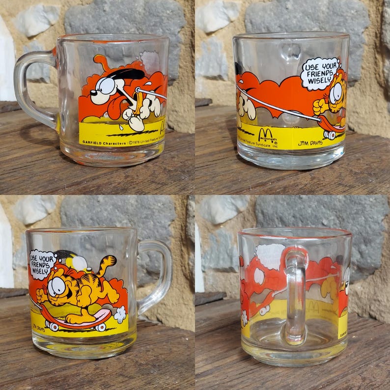 May include: Four clear glass mugs with a Garfield cartoon character design. The mugs feature a red, orange, and yellow color scheme. The text on the mugs reads "Use your friends wisely." and "Garfield Characters &copy;1978 United Feature Syndicate, Inc."