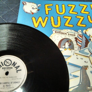 May include: A vintage vinyl record with a label from National Records, featuring the text "Takes You to Farmland" and "Barnyard Carnival of Animals." Beside it is a children's book cover titled "Fuzzy Wuzzy" with illustrations of a polar bear, penguin, and seal.