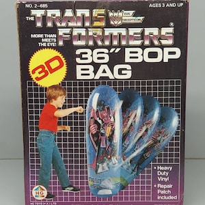 May include: A box for a 36-inch Transformers Bop Bag. The box is purple and black with a picture of a boy punching the bag. The bag is blue and white with a picture of Optimus Prime on it. The box says "More than meets the eye!" and "Evil Decepticon".