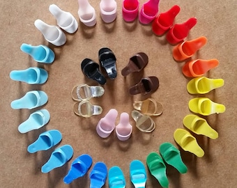 May include: A colorful assortment of miniature doll shoes arranged in a spiral. The collection includes various styles like sandals and heels, in a spectrum of colors such as blue, pink, red, and yellow. The shoes are made of plastic and other materials.