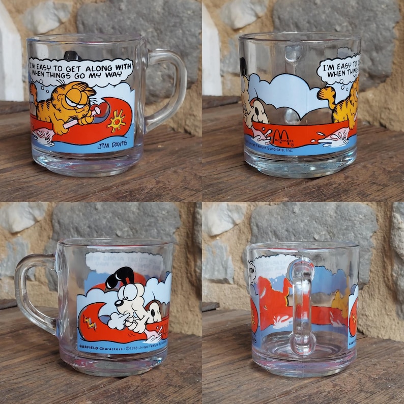 May include: Four clear glass mugs with a Garfield cartoon design. The mugs feature Garfield in a red boat with the text "I'm easy to get along with when things go my way".