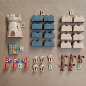Pode incluir: Um conjunto de construção de castelo com uma torre, muros e portões. Há também pequenas figuras de cavaleiros e bandeiras. O conjunto inclui as etiquetas A1, B3, C3, D2, E1, F4 e G2.