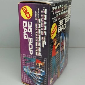 May include: A cardboard box for a Transformers 36-inch Bop Bag. The box is purple and features a 3D image of the Transformers logo and a robot. The box also has the text "The Transformers" and "More Than Meets The Eye!" printed on it.