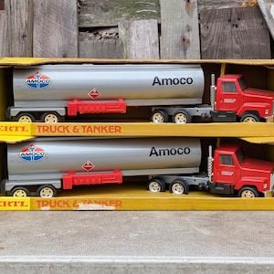 Puede incluir: Dos camiones cisterna de juguete Amoco en sus cajas amarillas originales. Los camiones tienen cabinas rojas y tanques plateados con el logotipo de Amoco. Las cajas dicen "Ertl Truck & Tanker".