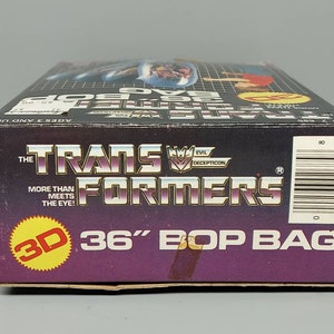 May include: A purple and black box with a 3D image of a robot on the front. The box is labeled "The Transformers 36" Bop Bag".