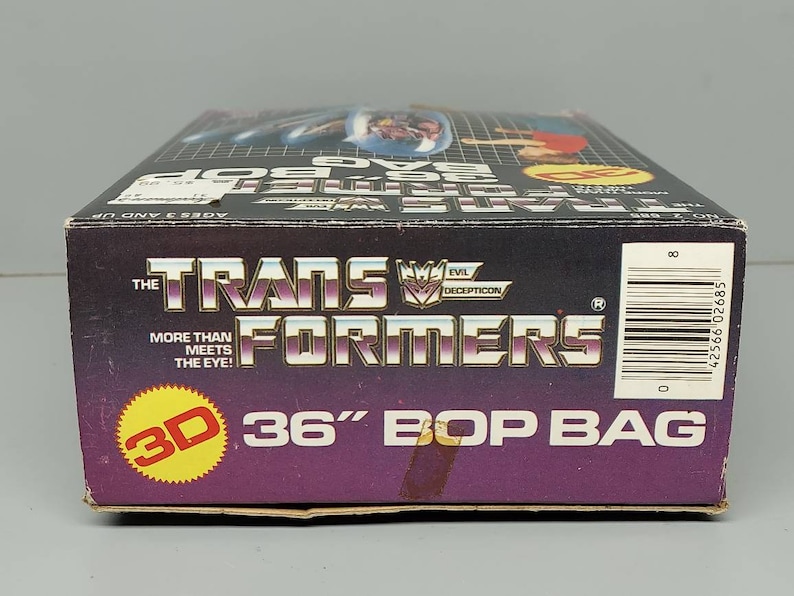 May include: A purple and black box with a 3D image of a robot on the front. The box is labeled "The Transformers 36" Bop Bag".