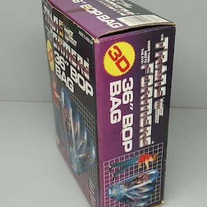 May include: A purple and yellow box for a 36-inch Transformers Bop Bag. The box features a 3D image of the Transformers logo and a character from the Transformers cartoon. The text on the box reads "Transformers 36" Bop Bag".