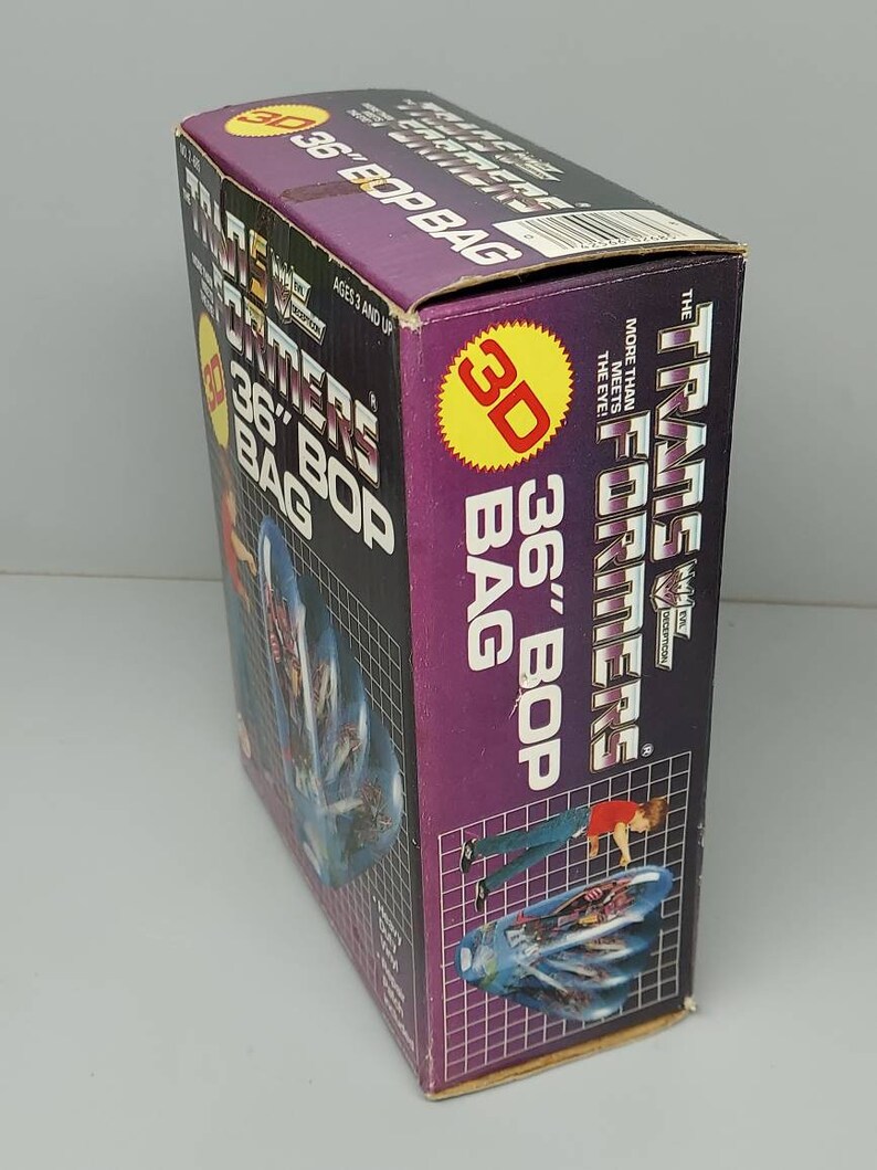 May include: A purple and yellow box for a 36-inch Transformers Bop Bag. The box features a 3D image of the Transformers logo and a character from the Transformers cartoon. The text on the box reads "Transformers 36" Bop Bag".