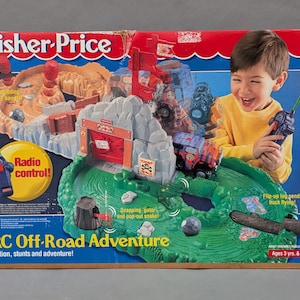 May include: A Fisher-Price RC Off-Road Adventure playset box. The box features a colorful illustration of a child playing with a remote control truck on a green and brown track with a rock formation and a red gate. The box reads "Radio control!" and "Ages 3 yrs. & up."