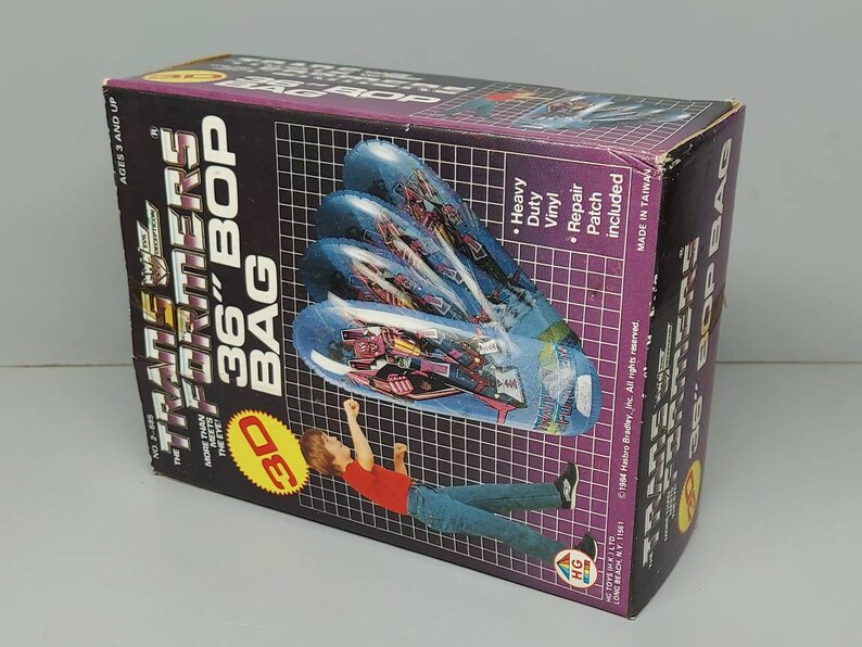May include: A Transformers 36-inch inflatable bop bag with a 3D image of a robot. The bag is purple, blue, and black. The box is black with white text and a picture of a child kicking the bag.