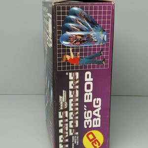 May include: A cardboard box with a purple background and the text "The Transformers 36" Bop Bag" in white. The box features a 3D image of a blue and silver robot.