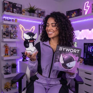 Puede incluir: Una figura redonda del personaje Gastly en blanco y negro que emerge de una base de Poké Ball blanca y roja, sostenida junto a una caja de cartón cuadrada con el texto BYWORT y una ilustración gráfica del mismo personaje en el frente.