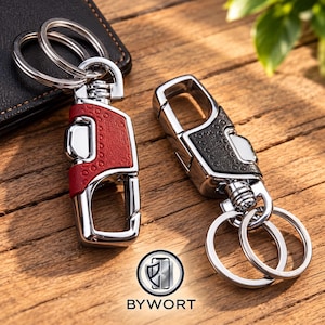 May include: Two metal keychains with polished silver-tone hardware and textured leather-like inserts. One keychain features a red insert, and the other features a black insert. Each includes a spring-loaded clasp and two circular split rings.