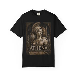 May include: A black short-sleeve t-shirt featuring a sepia-toned graphic print of Athena wearing a helmet, accompanied by an owl. The text reads ATHENA GODDESS OF WISDOM & WAR STRATEGY. The design includes architectural elements and laurel leaves.