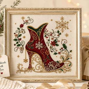 May include: A framed cross-stitch embroidery featuring a deep red high-heeled boot decorated with gold filigree, green holly leaves, and white snowflakes. The design is set against a cream-colored fabric background within a metallic gold frame.