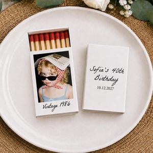 May include: Two white matchboxes with red-tipped matches. One box features a photograph of a child wearing sunglasses and a red checkered headscarf with the text Vintage 1986. The other box displays the text Sofia's 40th Birthday and 10.12.2027.