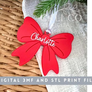 Puede incluir: Un adorno de color rojo brillante con forma de lazo que presenta el nombre Charlotte en letras cursivas blancas. El adorno incluye un pequeño lazo en la parte superior con una cinta blanca para colgarlo. El texto DIGITAL 3MF AND STL PRINT FILE es visible.