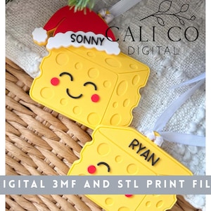 Puede incluir: Dos adornos amarillos con forma de queso y agujeros, cada uno con una cara sonriente y mejillas rojas. Un adorno lleva un gorro de Papá Noel rojo y blanco con el nombre SONNY, y el otro tiene el nombre RYAN. El texto dice CALI CO DIGITAL.
