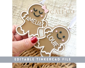 May include: Two gingerbread-shaped ornaments in tan with white icing-style borders. One features a pink bow, closed eyes, and the name AMELIA. The other has open eyes and the name LOUIE. Both have white ribbons for hanging and text reading CALI CO DIGITAL.