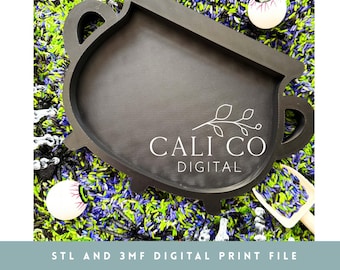以下が含まれることがあります： 2つのサイドハンドルが付いた黒い大釜型のトレイで、白い文字でCALI CO DIGITALと葉のグラフィックが描かれています。トレイは紫、緑、黒の米の上に置かれ、プラスチック製の目玉と小さな白いスクープが散らばっています。