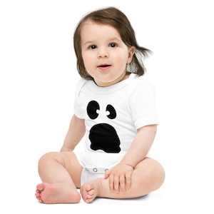 Puede incluir: Un body blanco de manga corta para bebé con un estampado gráfico negro de una cara de fantasma, que presenta dos ojos ovalados y una boca circular grande e irregular. La prenda tiene un cuello redondo y cierres a presión.
