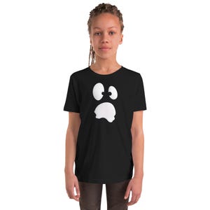Puede incluir: Una camiseta negra de manga corta con un gráfico blanco grande y centrado que representa un rostro sorprendido o asustado, con dos ojos redondos y muy abiertos y una boca abierta con bordes ondulados sobre la tela negra lisa.