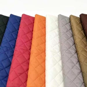 May include: A collection of quilted fabric swatches arranged in a row, featuring a variety of colours including black, blue, red, orange, white, grey, tan, and dark brown, all displaying a consistent diamond-shaped stitched pattern throughout.