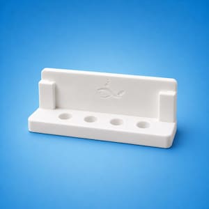 May include: A white rectangular stand featuring a raised back panel with an embossed fish icon and three small bubbles above it. The base includes four circular indentations arranged in a horizontal row, flanked by two vertical side supports.