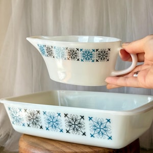 Peut inclure: Une saucière et un plat de cuisson rectangulaire en verre opalin blanc, tous deux ornés d'un motif répétitif de fleurs stylisées bleues et noires disposées en bande horizontale sur l'extérieur de chaque pièce.