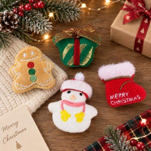 May include: Four felt Christmas ornaments including a tan gingerbread person with three buttons, a green gift box with a gold ribbon, a white snowman with a pink hat and scarf, and a red stocking with the text Merry Christmas embroidered in white.